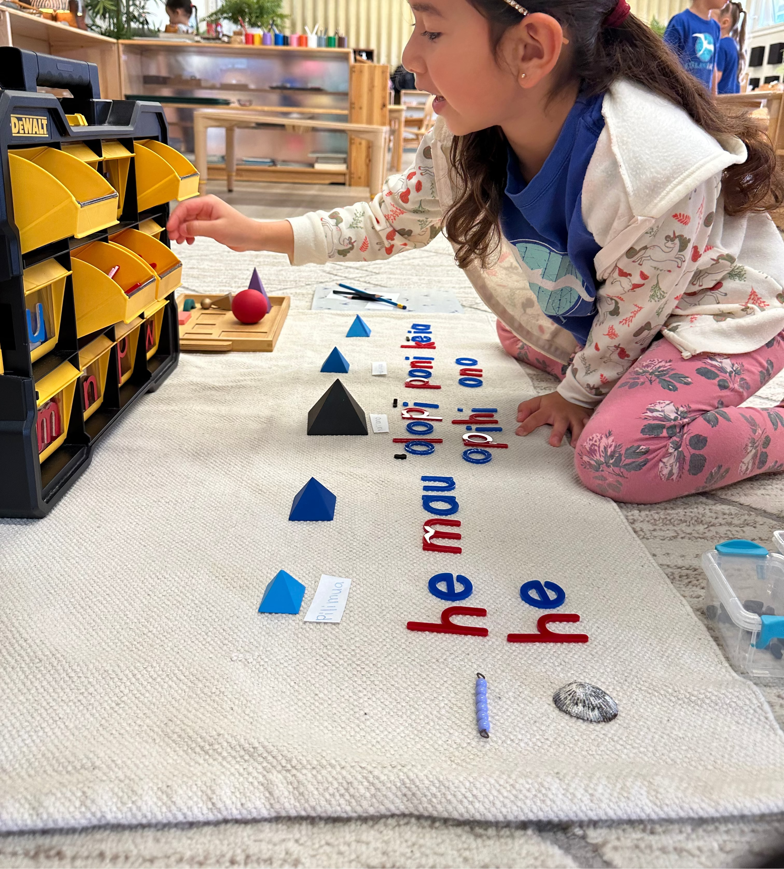 Child playing with hawaiian educational toys on a mat with letters in a classroom setting