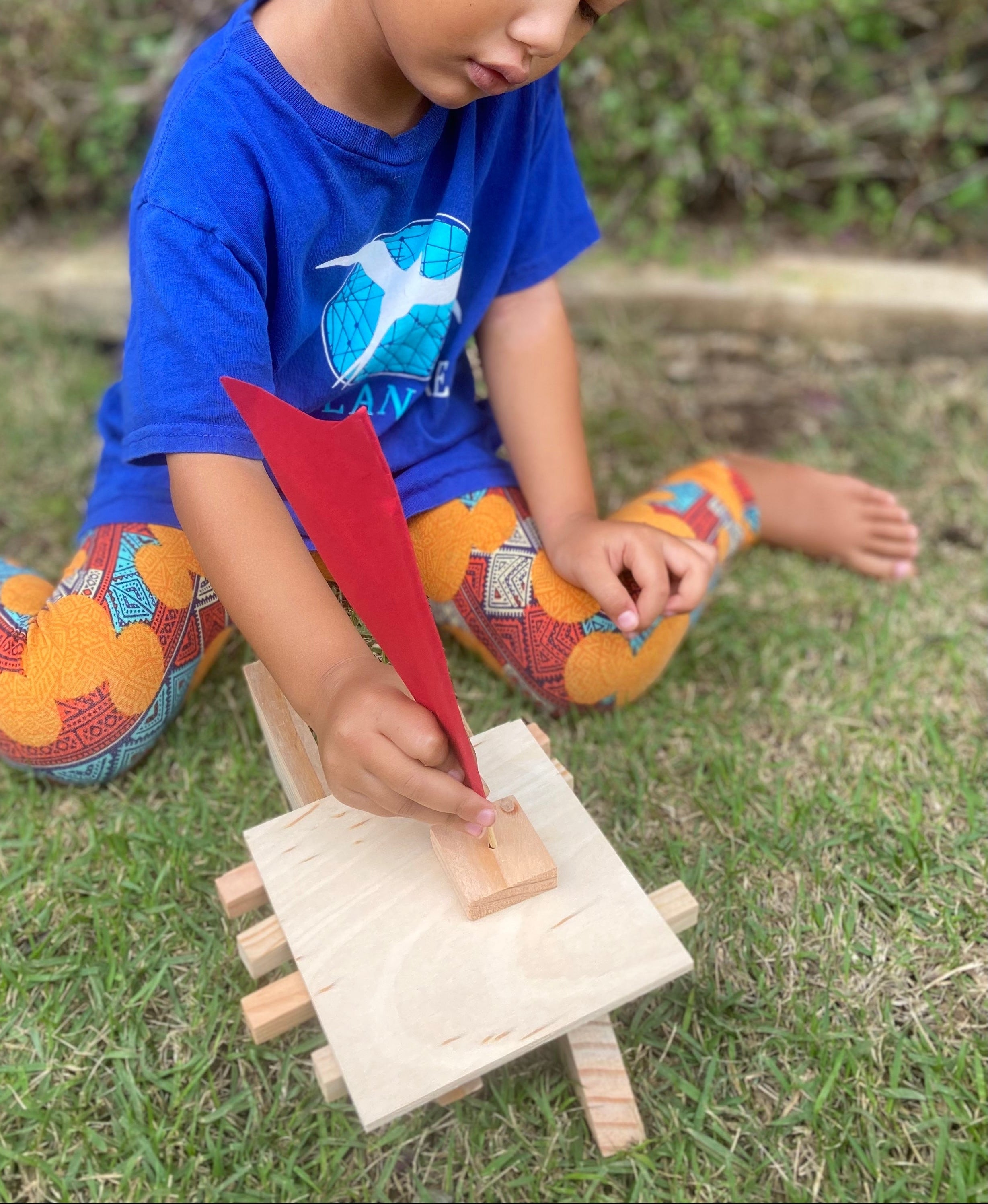 Child playing with a wooden hawaiian canoe outdoors on grass